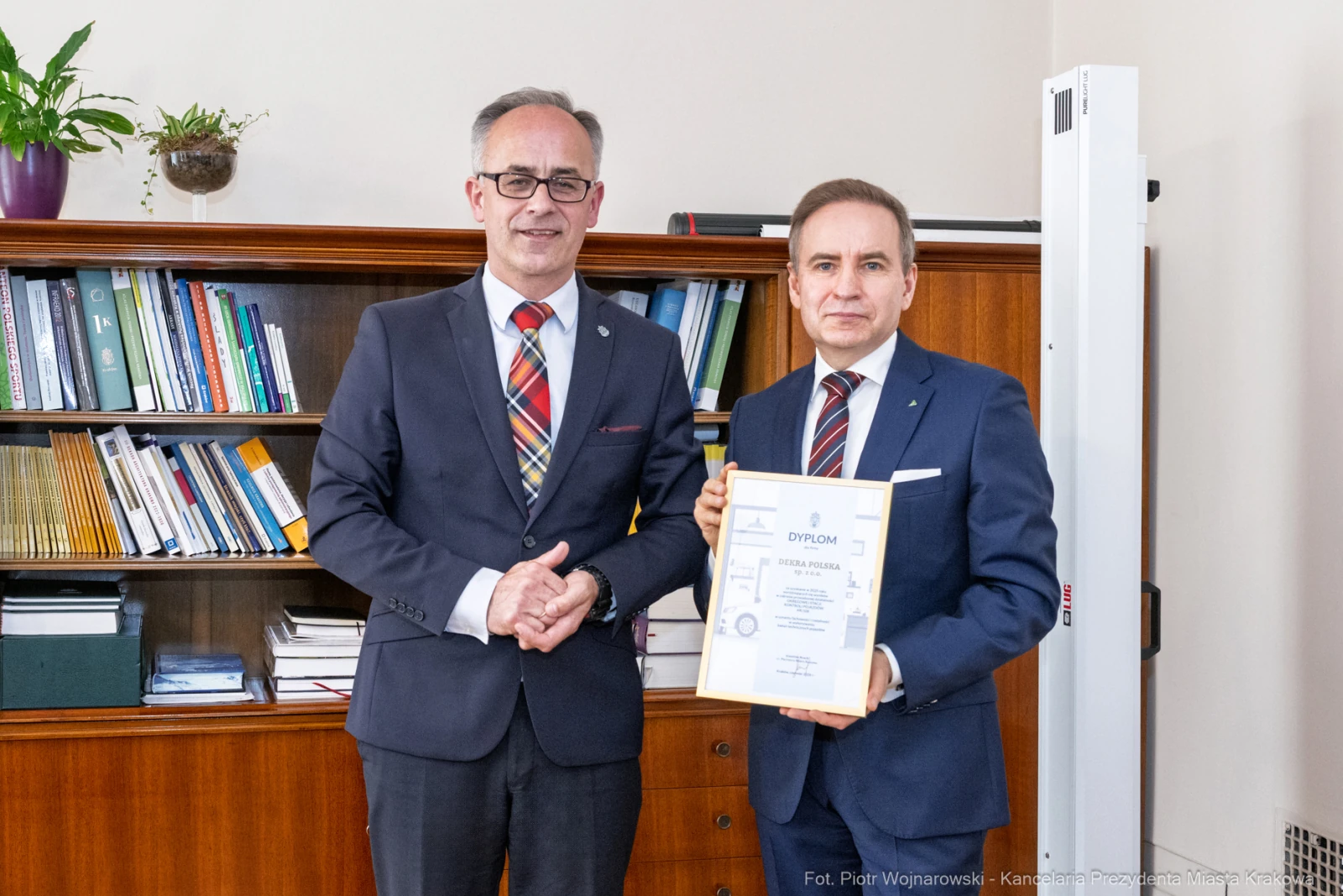 Dwóch mężczyzn trzyma dyplom w biurze, w tle półki z książkami.  Autor: Piotr Wojnarowski