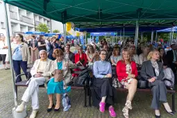 Grupa osób siedzących pod zielonymi namiotami, uśmiechających się i rozmawiających.