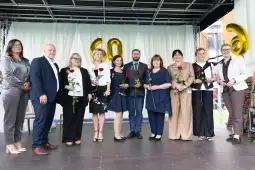 Grupa osób z różnymi kwiatami na scenie, świętujących jubileusz.