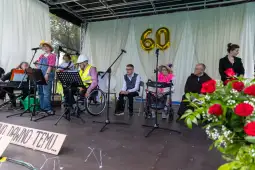 Uczestnicy wydarzenia na scenie, obchody 60-lecia, kwiaty w tle.