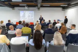 Prezentacja w sali konferencyjnej z uczestnikami siedzącymi na krzesłach.