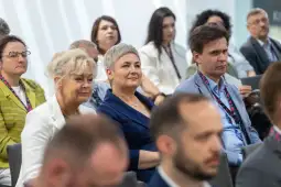 Grupa ludzi siedzących na konferencji, skupionych na prelekcji.