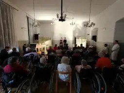 Występ artystyczny dla seniorów w sali z widownią na wózkach inwalidzkich.