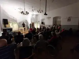 Występ artystyczny dla osób starszych w sali z widownią na wózkach inwalidzkich.