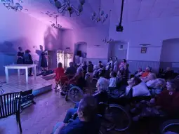 Występ artystyczny dla osób starszych w sali z widownią na wózkach inwalidzkich.