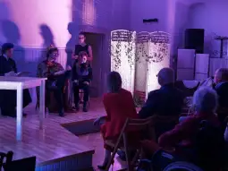 Spektakl teatralny z aktorami w kostiumach, widownia obserwująca przedstawienie.