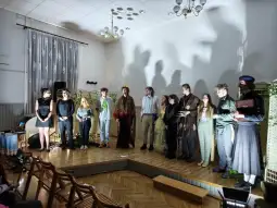 Grupa osób na scenie podczas występu teatralnego, z cieniami rzucanymi na ścianę.