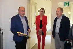 Mężczyzna przemawia, obok niego kobieta w czerwonym garniturze i starszy mężczyzna.