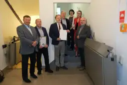 Grupa osób stojąca na schodach, trzymająca dyplomy i nagrody.