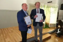 Dwaj mężczyźni trzymają dyplomy i uśmiechają się w eleganckim wnętrzu.
