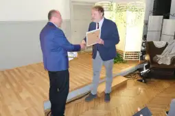 Dwóch mężczyzn uścisnęło sobie ręce, jeden wręcza drugiemu dyplom.
