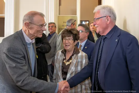 Spotkanie trzech osób, uściski dłoni, rozmowy w tle.