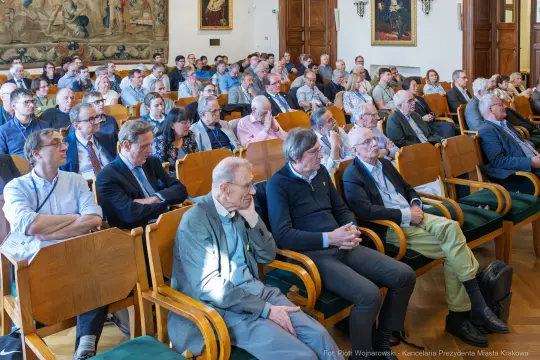 Zgromadzenie ludzi w sali, słuchających prelekcji lub wykładu.