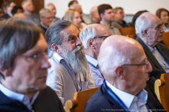 Grupa mężczyzn w sali konferencyjnej, niektórzy z brodami, słuchających prelekcji.