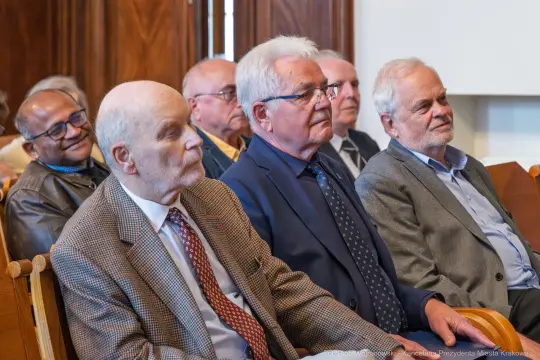 Grupa mężczyzn siedzących w sali, słuchających wykładu lub prezentacji.