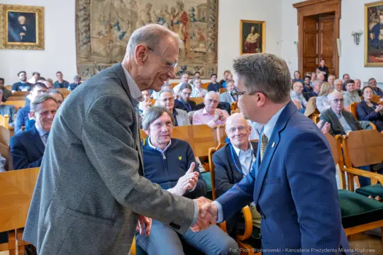 Spotkanie dwóch mężczyzn podczas wydarzenia w sali z publicznością.