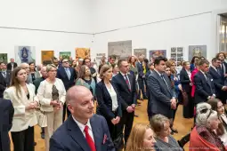Grupa ludzi w eleganckich strojach podczas wydarzenia kulturalnego w galerii sztuki.
