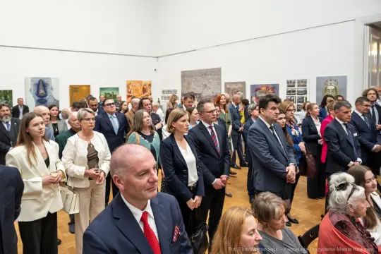 Grupa ludzi w eleganckich strojach podczas wydarzenia kulturalnego w galerii sztuki.