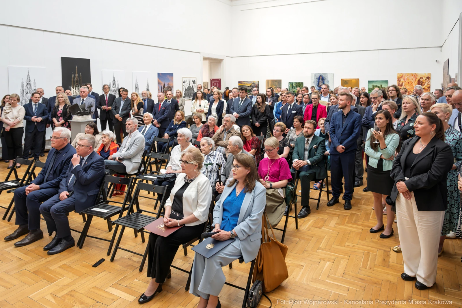 Tłum ludzi w sali wystawowej, siedzących na krzesłach, w eleganckich strojach.  Autor: Piotr Wojnarowski