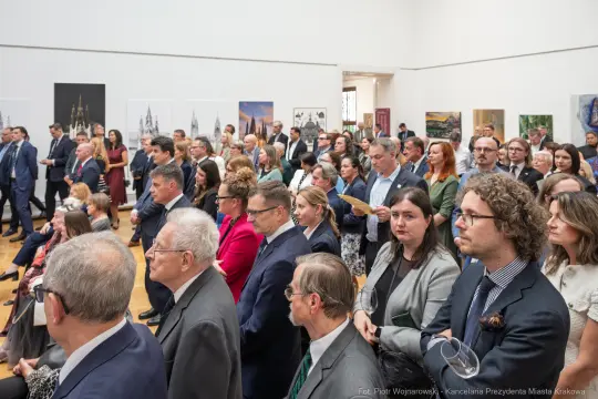 Tłum ludzi w eleganckich strojach podczas wydarzenia kulturalnego w galerii.