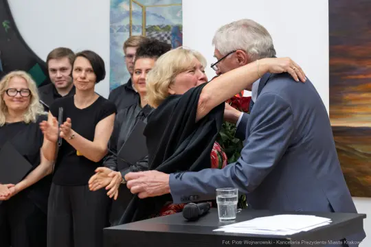 Uścisk dłoni między dwiema osobami, w tle grupa ludzi, atmosfera radości i celebracji.