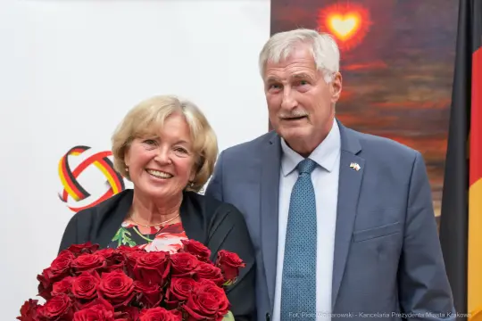 Para uśmiechniętych ludzi trzymająca bukiet czerwonych róż.