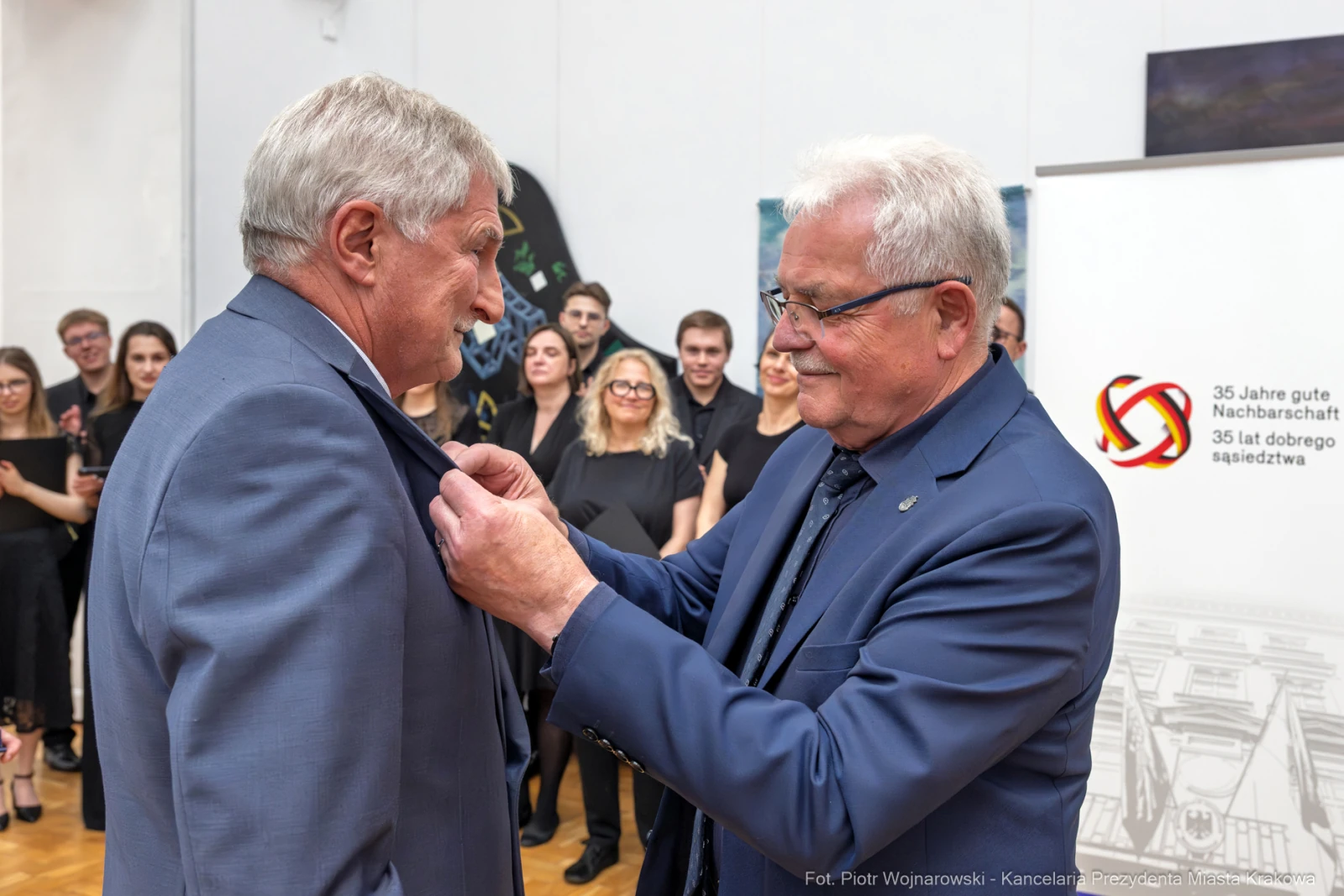 Mężczyzna przypina odznaczenie do marynarki innego mężczyzny podczas uroczystości.  Autor: Piotr Wojnarowski