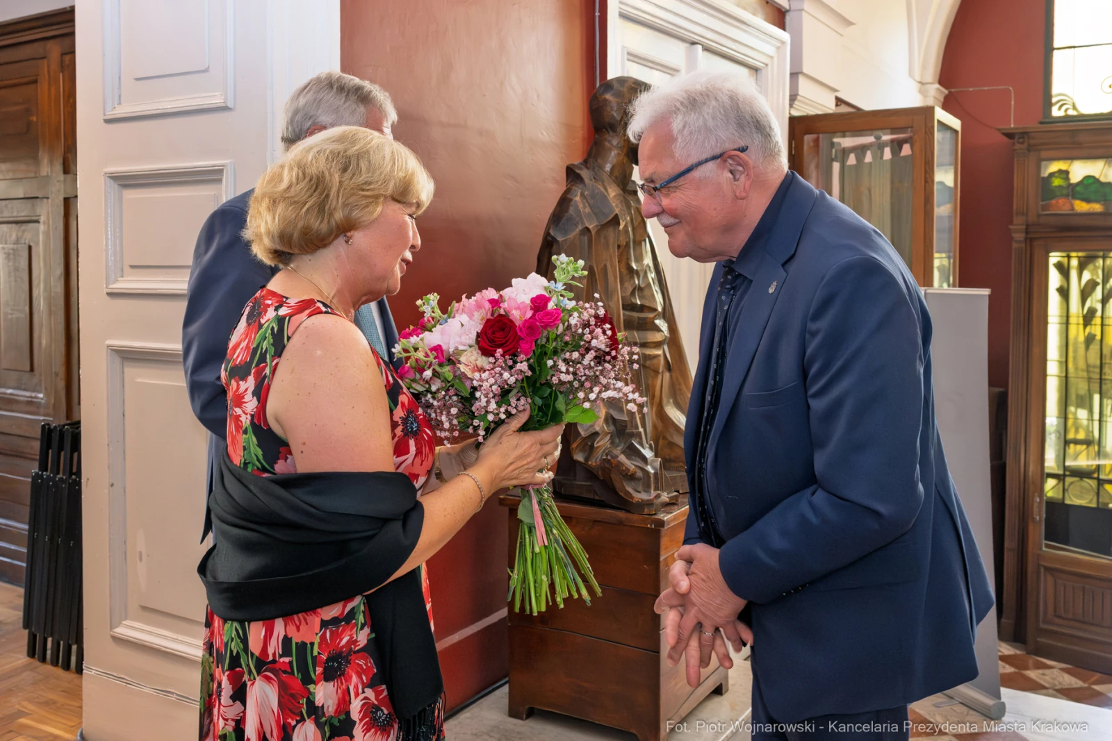 Kobieta wręcza bukiet kwiatów mężczyźnie w eleganckim otoczeniu.  Autor: Piotr Wojnarowski