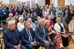 Grupa ludzi w formalnych strojach podczas wydarzenia kulturalnego w sali wystawowej.