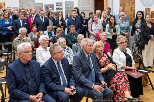 Grupa ludzi w formalnych strojach podczas wydarzenia kulturalnego w sali wystawowej.