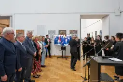 Uroczystość z wystąpieniem i chórem w tle, uczestnicy w eleganckich strojach.