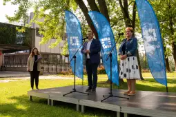 Konferencja prasowa z mówcami przy mikrofonach i flagami w tle.