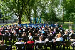 Grupa dzieci siedzących na krzesłach w parku, zorganizowane wydarzenie na świeżym powietrzu.