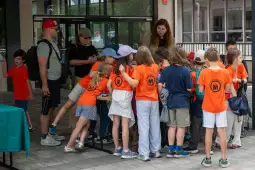 Grupa dzieci w pomarańczowych koszulkach zbiera się wokół stołu.