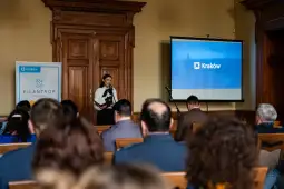 Prezentacja w sali konferencyjnej z osobą mówiącą do publiczności.