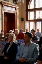 Grupa ludzi siedzących w sali podczas wydarzenia.