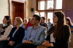 Grupa osób siedzących w sali, skupionych na prelekcji.