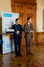 Dwóch mężczyzn w formalnych strojach podczas uroczystości wręczenia nagrody w Krakowie.