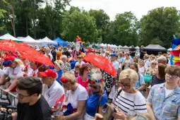 Tłum ludzi z parasolkami w kolorowych strojach, uczestniczących w festiwalu na świeżym powietrzu.