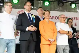 Grupa osób na scenie podczas wydarzenia, w tym mężczyzna w garniturze i kobieta w pomarańczowym garniturze.