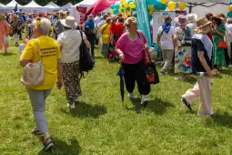 Grupa osób w kolorowych strojach na festynie, wśród zielonej trawy i dekoracji.