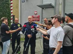 Mężczyzna w mundurze udziela wywiadu otoczony przez dziennikarzy z mikrofonami.
