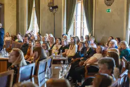 Grupa kobiet siedzących w sali konferencyjnej, słuchających prelekcji.