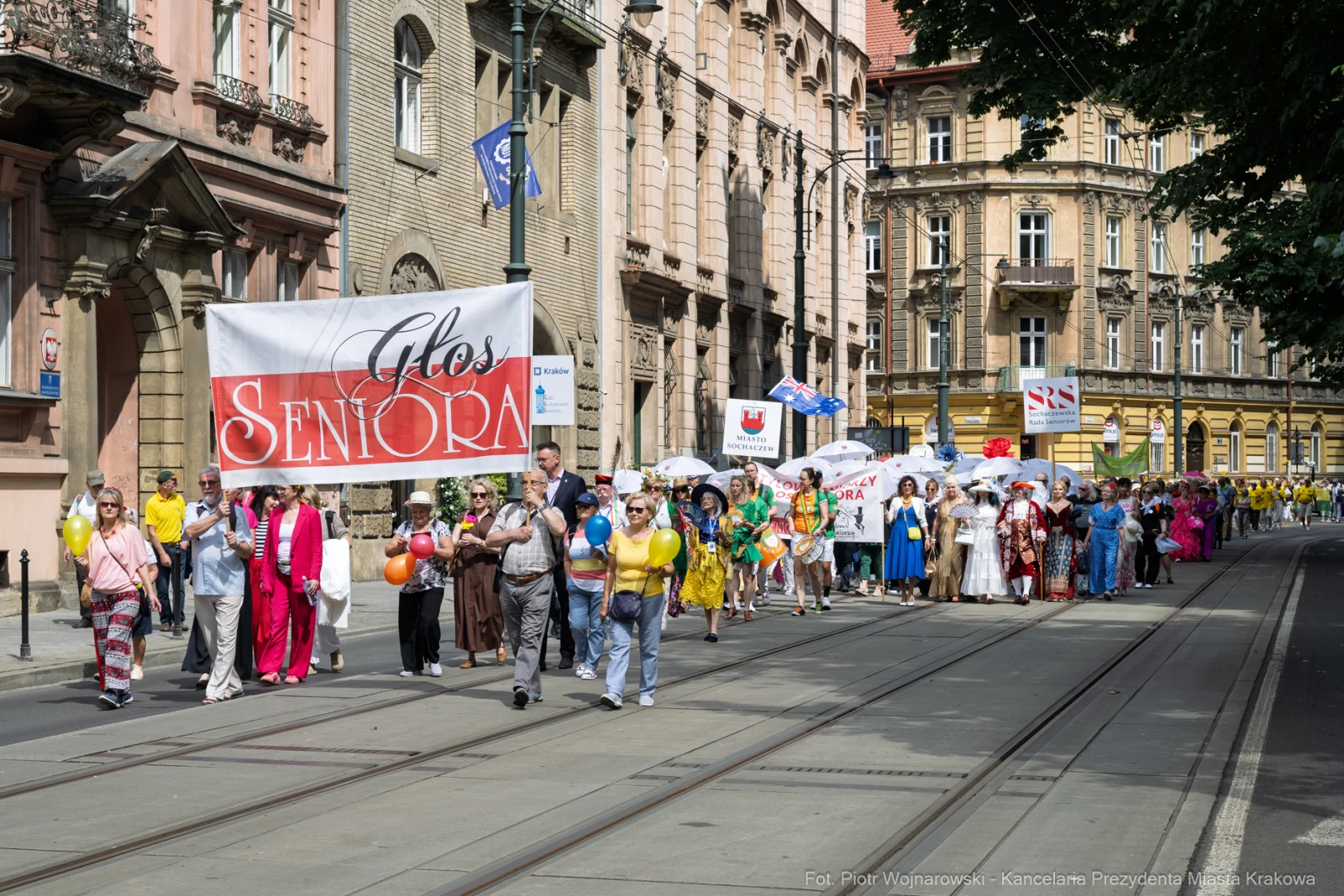 Parada seniorów w kolorowych strojach na ulicach Krakowa. Transparenty i balony w tle.  Autor: Piotr Wojnarowski