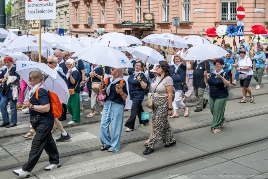 Grupa seniorów idąca w marszu z parasolami, niosąca transparenty.