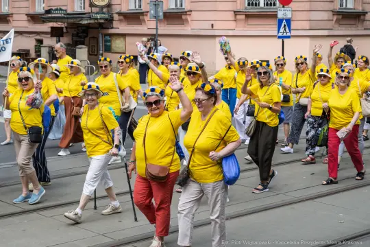 Grupa osób w żółtych koszulkach maszeruje, machając rękami i uśmiechając się.