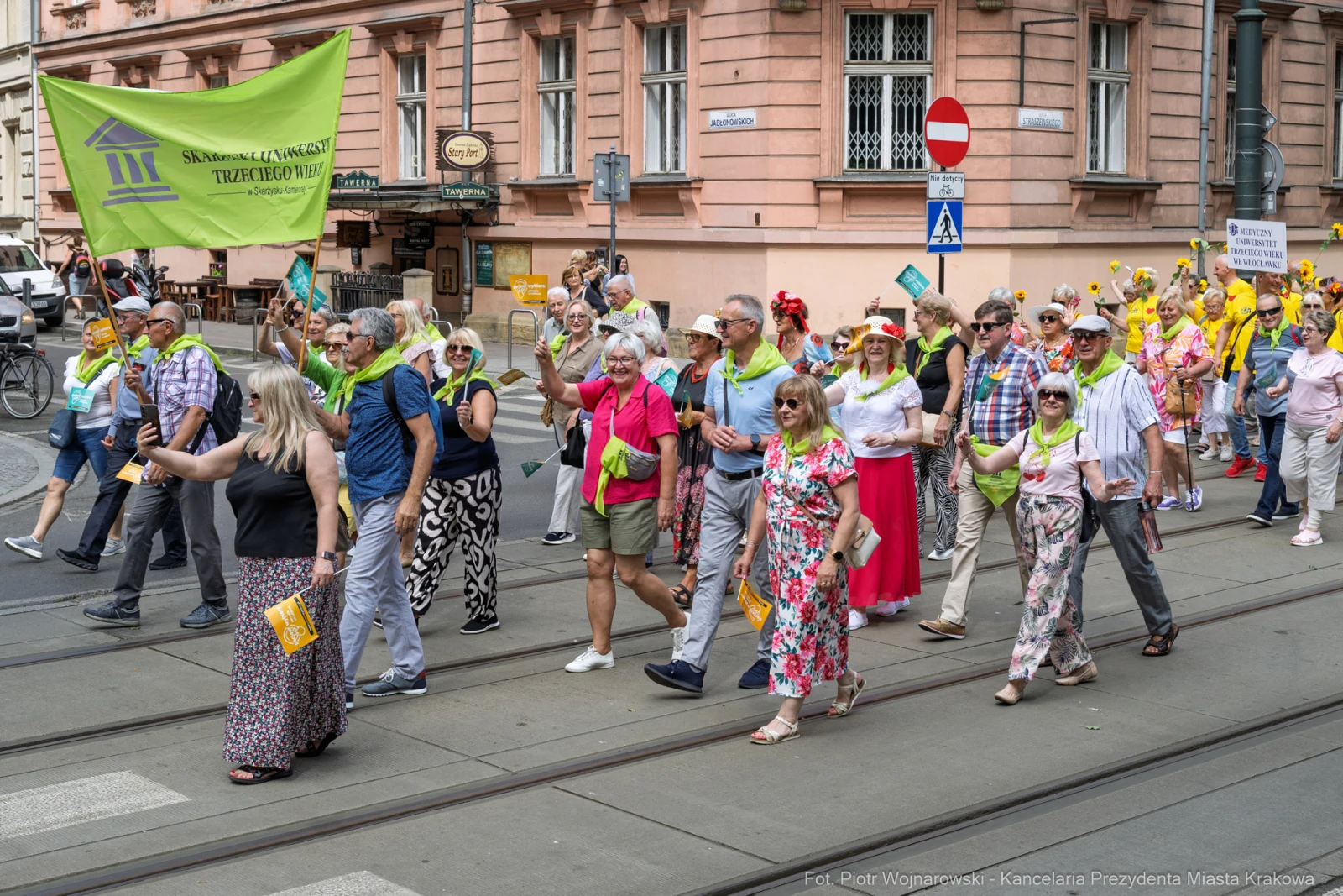 Grupa osób w kolorowych strojach maszeruje ulicą, trzymając flagi i transparenty.  Autor: Piotr Wojnarowski