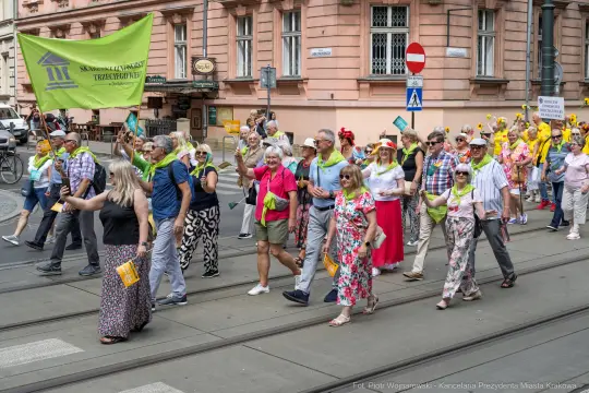 Grupa osób w kolorowych strojach maszeruje ulicą, trzymając flagi i transparenty.