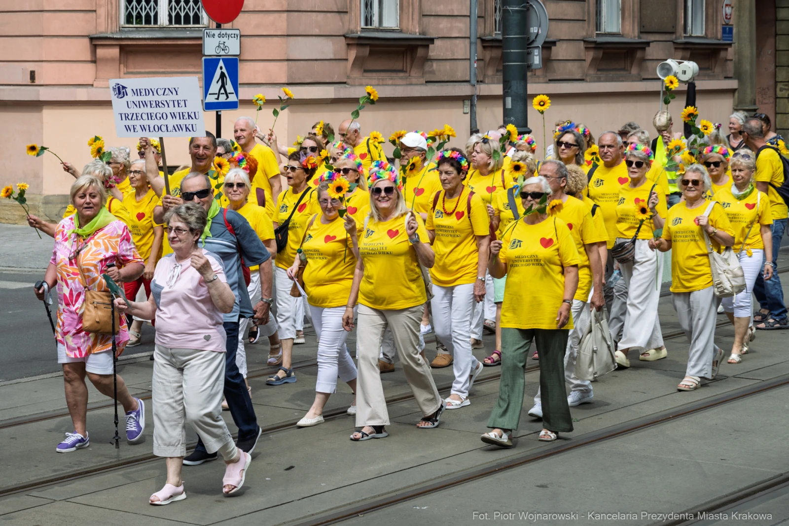 Grupa osób w żółtych koszulkach z kwiatami na głowach maszeruje ulicą.  Autor: Piotr Wojnarowski