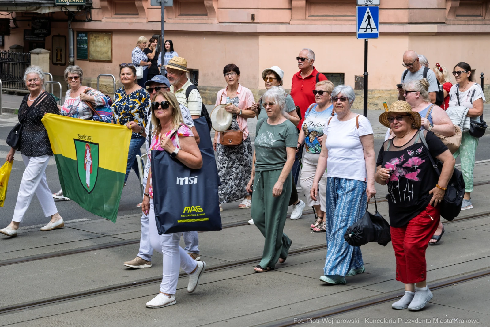 Grupa osób spacerujących po ulicy, niektóre trzymają flagi i torby.  Autor: Piotr Wojnarowski